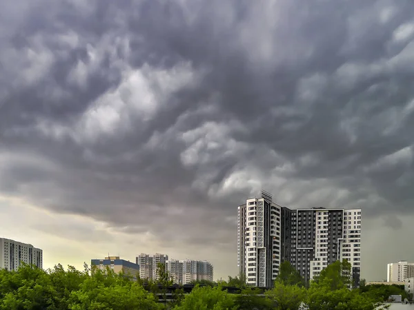An ominous stormy sky with clubs of gray heavy clouds over multi-story city houses. Natural spontaneous phenomenon.