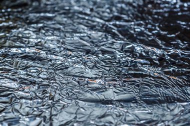 Buruşmuş alüminyum folyonun arkaplan dokusunun bir parçası üzerine seçici bir odaklanma. Parlak buruşuk yüzey.