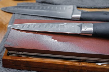 Su değirmeni taşının üzerinde duran çelik mutfak bıçağına odaklan. Ustura keskinliği için bıçak keskinleştirme işlemi. Şeffaf bir su damlasının üzerinde. 