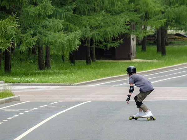 Rückansicht eines Mannes in schwarzer Uniform, der sich mit hoher Geschwindigkeit auf einem Longboard bewegt. — Stockfoto