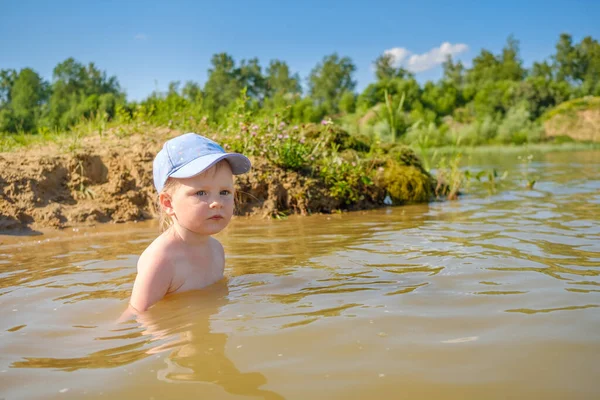 Маленькая блондинка в кепке купается в реке и весело смеется. Копирование пространства. Стоковое Изображение