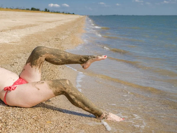 Vista de hermosos pies femeninos con pedicura roja brillante en la arena de la playa. Los tobillos de los pies están untados con lodo curativo. Rejuvenecimiento de la piel mientras se relaja en el mar. Spa. Copiar espacio — Foto de Stock