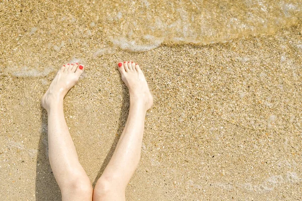 Vista dall'alto di bei piedi femminili con pedicure rosso brillante sulla sabbia della spiaggia. L'onda del mare lava i piedi alle donne. Relax e divertimento durante la vostra vacanza al mare. Copia spazio. — Foto Stock