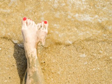 Sahilin kumlarında parlak kırmızı pedikürlü güzel kadın ayaklarının manzarası. Ayak bileklerinde tıbbi çamur lekesi var. Denizde dinlenirken cilt tazeleme. Spa mı? Boşluğu kopyala