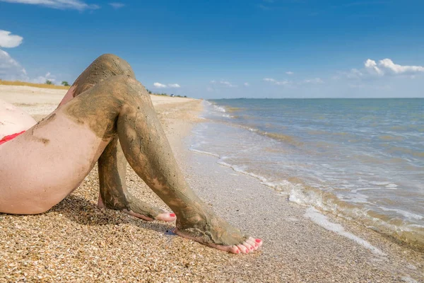 Vy över vackra kvinnliga fötter med ljusa röda pedikyr på sanden på stranden. Fötternas vrister är utsmetade med läkande lera. Hudföryngring samtidigt som du kopplar av till havs. Ett spa. Kopiera utrymme — Stockfoto