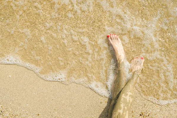 Vista dall'alto di bei piedi femminili con pedicure rosso brillante sulla sabbia della spiaggia. Le caviglie dei piedi sono imbrattate di fango medicinale. Ringiovanimento della pelle durante il relax in mare. Spa. Copia spazio — Foto Stock