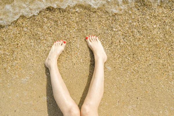 Vista dall'alto di bei piedi femminili con pedicure rosso brillante sulla sabbia della spiaggia. L'onda del mare lava i piedi alle donne. Relax e divertimento durante la vostra vacanza al mare. Copia spazio. — Foto Stock