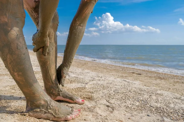 选择关注美丽的雌性脚，并在沙滩上做鲜红色的足底修整。双手沾满了足踝上的淤泥.在海上放松的同时使皮肤年轻化。SPA 。复制空间 — 图库照片