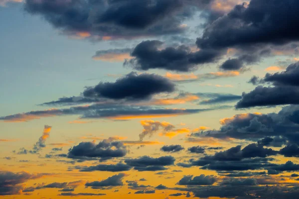 A very dramatic sky full of yellows, blues and oranges. Contrasting clouds during sunset illuminated by the setting sun. Bright saturated natural background. — Stock Photo, Image