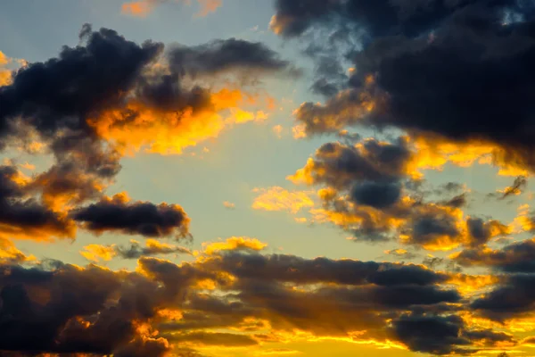 A very dramatic sky full of yellows, blues and oranges. Contrasting clouds during sunset illuminated by the setting sun. Bright saturated natural background. — Stock Photo, Image