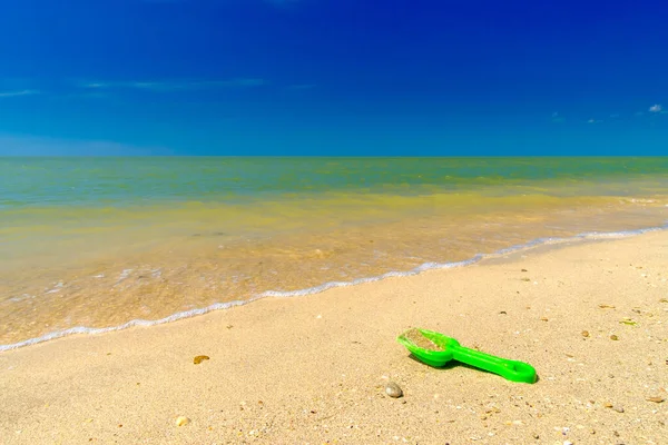 Зелений пластиковий дитячий садок в піску на морському пляжі. Концепція морської відпустки з дітьми під час відпустки. Літній сонячний день на морському курорті. Блакитне небо і спокійне море. Копіювати простір — стокове фото