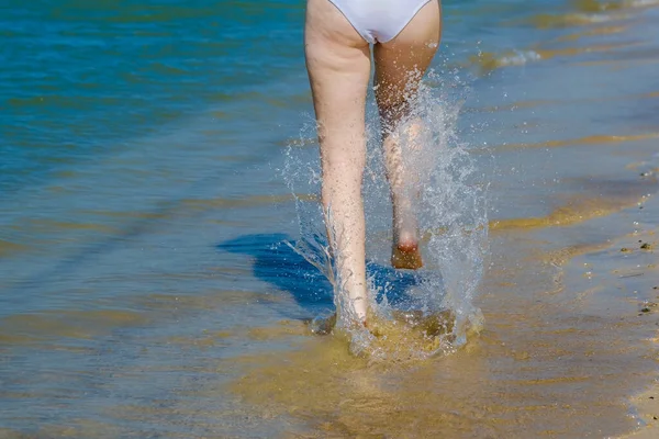 Piękne nogi młodej dziewczyny biegającej po wodzie na piaszczystej plaży. Fala rozbija się na dziewczęcych nogach. Upiorna woda morska i morska piana u twych stóp. Koncepcja podróży — Zdjęcie stockowe