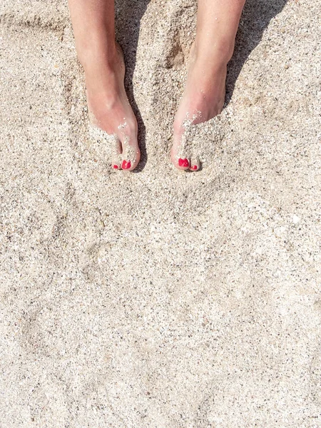 Vista dall'alto delle gambe femminili con pedicure rosse nella sabbia della spiaggia. Riposo e ricreazione in mare. Copia spazio. — Foto Stock