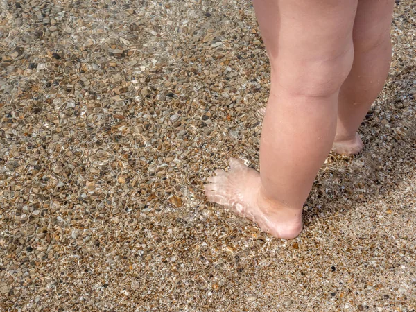 Baby piedi primo piano sulla sabbia della spiaggia del mare. L'acqua di mare lava i piedi. Buona infanzia. Riposa al mare. Giornata estiva di sole. Copia spazio — Foto Stock
