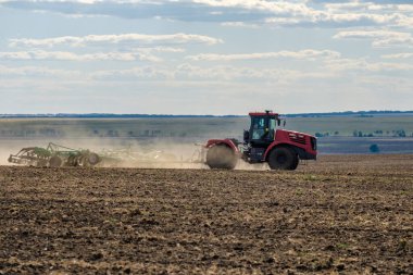 Toz bulutundaki kırmızı bir çiftlik traktörü, hasattan sonra tarladaki toprağı ekiciyle işliyor. Yaz güneşli bir gün. Bereketli topraklar. Modern tarım makineleri. Boşluğu kopyala.