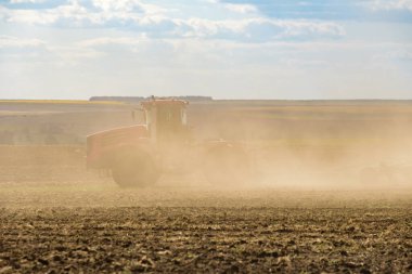 Toz bulutundaki kırmızı bir çiftlik traktörü, hasattan sonra tarladaki toprağı ekiciyle işliyor. Yaz güneşli bir gün. Bereketli topraklar. Modern tarım makineleri. Boşluğu kopyala.