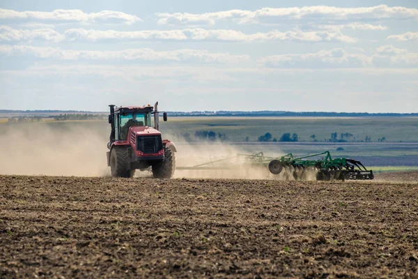 Toz bulutundaki kırmızı bir çiftlik traktörü, hasattan sonra tarladaki toprağı ekiciyle işliyor. Yaz güneşli bir gün. Bereketli topraklar. Modern tarım makineleri. Boşluğu kopyala.