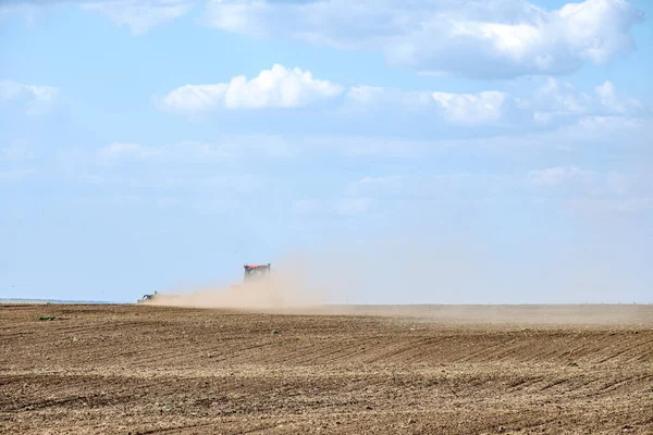 Um trator de fazenda vermelho em uma nuvem de poeira cultiva o solo no campo com um cultivador após a colheita. Dia ensolarado de verão. Terra fértil. Máquinas agrícolas modernas. Espaço de cópia. — Fotografia de Stock