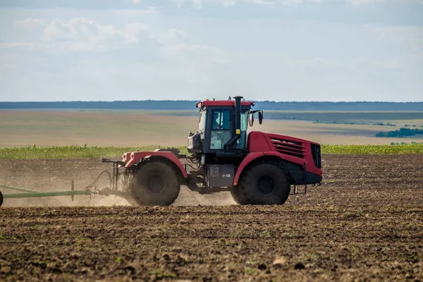 Un tractor rojo de granja en una nube de polvo cultiva el suelo en el campo con un cultivador después de la cosecha. Día soleado de verano. Tierra fértil. Maquinaria agrícola moderna. Copiar espacio. —  Fotos de Stock