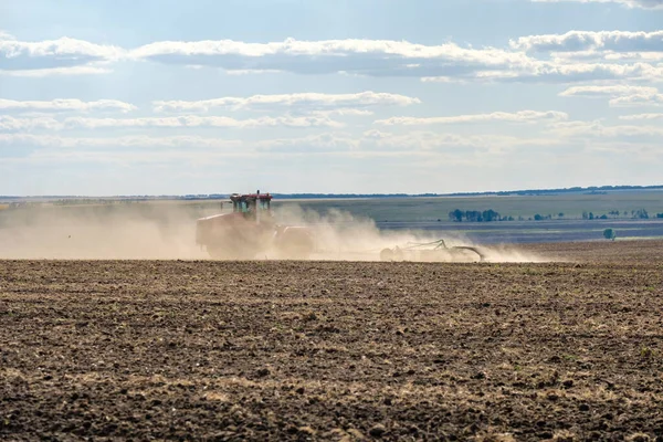 Un tractor rojo de granja en una nube de polvo cultiva el suelo en el campo con un cultivador después de la cosecha. Día soleado de verano. Tierra fértil. Maquinaria agrícola moderna. Copiar espacio. —  Fotos de Stock