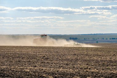 Toz bulutundaki kırmızı bir çiftlik traktörü, hasattan sonra tarladaki toprağı ekiciyle işliyor. Yaz güneşli bir gün. Bereketli topraklar. Modern tarım makineleri. Boşluğu kopyala.