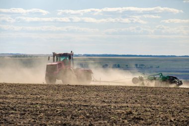 Toz bulutundaki kırmızı bir çiftlik traktörü, hasattan sonra tarladaki toprağı ekiciyle işliyor. Yaz güneşli bir gün. Bereketli topraklar. Modern tarım makineleri. Boşluğu kopyala.