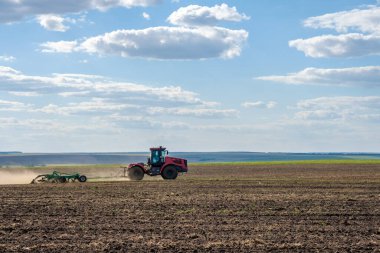 Toz bulutundaki kırmızı bir çiftlik traktörü, hasattan sonra tarladaki toprağı ekiciyle işliyor. Yaz güneşli bir gün. Bereketli topraklar. Modern tarım makineleri. Boşluğu kopyala.