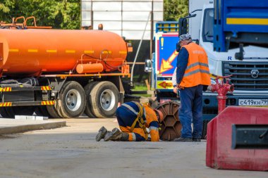 Moskova. - Rusya. 06 Eylül. Turuncu üniformalı ve koruyucu miğferli 2020 işçi kanalizasyon kapağından sokaklara servis yapıyor. Şehirdeki kamu hizmetlerinin işi.