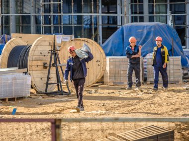 Moskova. - Rusya. İnşaat alanında üniformalı ve kasklı inşaat işçileri, inşaat malzemelerini elle transfer ediyorlar. Yaz günü. İnşaat endüstrisi