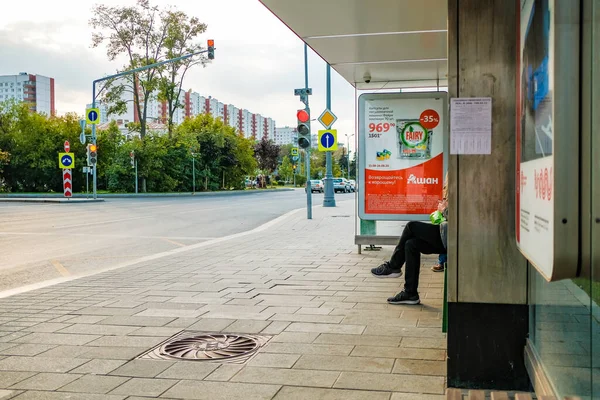 Moskau. Russland. 4. September 2020 Beine eines Mannes, der an einer Haltestelle des öffentlichen Nahverkehrs auf einer Bank sitzt. Warten auf die Ankunft des Busses. Sommertag — Stockfoto