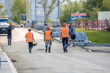 Moskova. - Rusya. 06 Eylül 2020 İnşaat malzemeleri arasında inşaat alanında yürüyen turuncu yelekli ve kasklı bir grup inşaat işçisinin görüntüsü