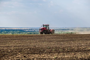 Toz bulutundaki kırmızı bir çiftlik traktörü, hasattan sonra tarladaki toprağı ekiciyle işliyor. Yaz güneşli bir gün. Bereketli topraklar. Modern tarım makineleri. Boşluğu kopyala.