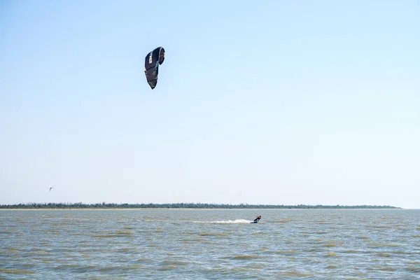 Yasenskaya trajekt. Rusko. 18. srpna2020. Atletický svalnatý opálený samec kitesurfer se řítí přes mořské vlny a skáče a v letním dni zvedá v jasném slunečním světle kapky vody. Extrémní sporty — Stock fotografie