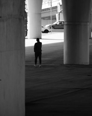 Bir yol köprüsünün altındaki dev beton sütunların arasında bir insan silueti. Büyük bir metropolde bir insanın önemsizliği kavramı. Işık ve gölgenin karşıtlığı. Siyah ve beyaz resim