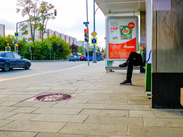 Moskau. Russland. 4. September 2020 Beine eines Mannes, der an einer Haltestelle des öffentlichen Nahverkehrs auf einer Bank sitzt. Warten auf die Ankunft des Busses. Sommertag — Stockfoto