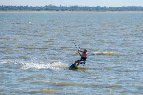 Yasenskaya trajekt. Rusko. 18. srpna2020. Atletický svalnatý opálený samec kitesurfer se řítí přes mořské vlny a skáče a v letním dni zvedá v jasném slunečním světle kapky vody. Extrémní sporty — Stock fotografie