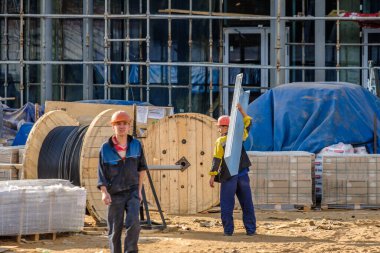 Moskova. - Rusya. İnşaat alanında üniformalı ve kasklı inşaat işçileri, inşaat malzemelerini elle transfer ediyorlar. Yaz günü. İnşaat endüstrisi