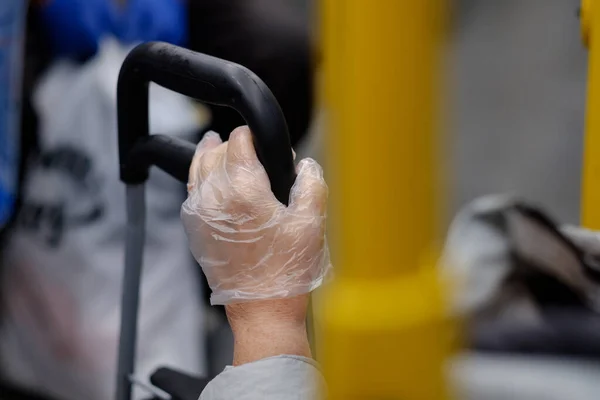 Szelektív fókusz egy női idős kézre egy műanyag kesztyűben, amely egy bőrönd nyelét fogja a tömegközlekedésben. — Stock Fotó