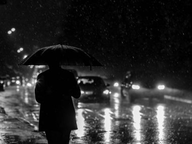 Gece sağanak yağış sırasında far ışığında şemsiyesi olan bir adamın silueti. Şehirde sağanak yağmur var