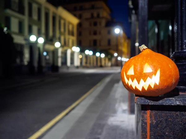 Halloween pumpkin on a deserted city street at night. Blurry colored city lights and old high-rise buildings. The decor of the night city in a festive Halloween theme. Copy space.