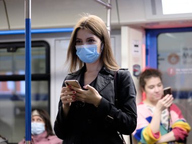 Moskova. - Rusya. 25 Eylül 2020 metro vagonunda genç bir kadın akıllı telefon tutuyor. Yolcuların yüzlerinde koruyucu maskeler var. Toplu taşımacılıktaki viral enfeksiyonlara karşı koruma.