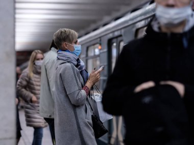 Moskova. - Rusya. 28 Eylül 2020. Koruyucu maskeli genç bir kız metro istasyonunun platformunda duruyor ve bir akıllı telefona coşkuyla bakıyor. Tren vagonları yakınlarda duruyor.. 