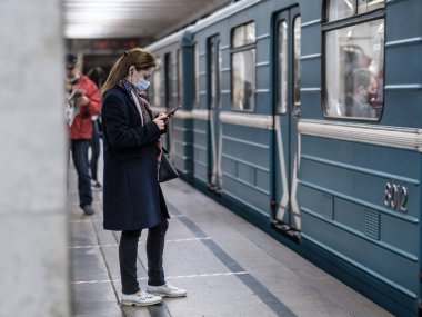 Moskova. - Rusya. 28 Eylül 2020. Koruyucu maskeli genç bir kız metro istasyonunun platformunda duruyor ve bir akıllı telefona coşkuyla bakıyor. Tren vagonları yakınlarda duruyor.. 