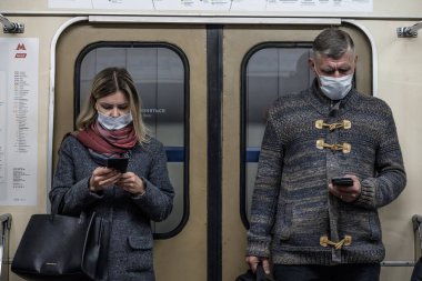 Moskova. - Rusya. 28 Eylül 2020 'de bir kadın ve koruyucu maskeli bir adam metro vagonunda durup akıllı telefonlarına bakıyorlar. Toplu taşımacılıktaki viral enfeksiyonlara karşı koruma.