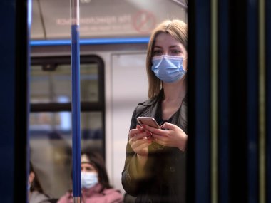 Moskova. - Rusya. 25 Eylül 2020 metro vagonunda genç bir kadın akıllı telefon tutuyor. Yolcuların yüzlerinde koruyucu maskeler var. Toplu taşımacılıktaki viral enfeksiyonlara karşı koruma.