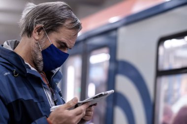 Moskova. - Rusya. 28 Eylül 2020. Koruyucu tıbbi maskeli bir adam metro istasyonunun platformunda duruyor ve dikkatle gazete okuyor. Koronavirüs salgınının ikinci dalgası..