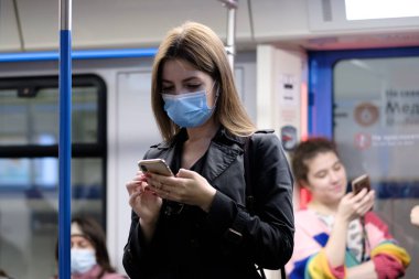 Moskova. - Rusya. 25 Eylül 2020 metro vagonunda genç bir kadın akıllı telefon tutuyor. Yolcuların yüzlerinde koruyucu maskeler var. Toplu taşımacılıktaki viral enfeksiyonlara karşı koruma.