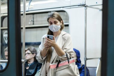 Moskova. - Rusya. 25 Eylül 2020 metro vagonunda genç bir kadın akıllı telefon tutuyor. Yolcuların yüzlerinde koruyucu maskeler var. Toplu taşımacılıktaki viral enfeksiyonlara karşı koruma.