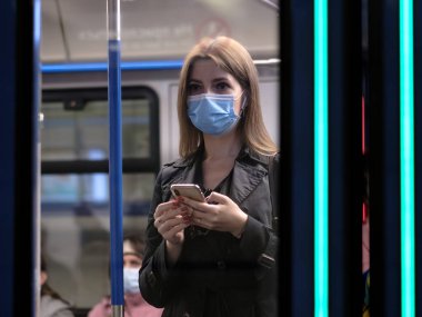 Moskova. - Rusya. 25 Eylül 2020 metro vagonunda genç bir kadın akıllı telefon tutuyor. Yolcuların yüzlerinde koruyucu maskeler var. Toplu taşımacılıktaki viral enfeksiyonlara karşı koruma.