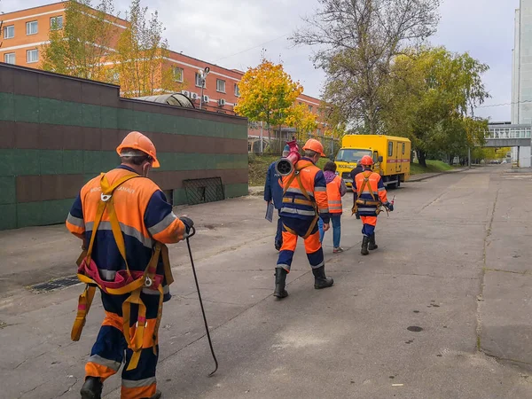 Moscou. La Russie. 7 octobre 2020. Les travailleurs en uniforme orange et casques marchent dans la rue en portant des outils — Photo